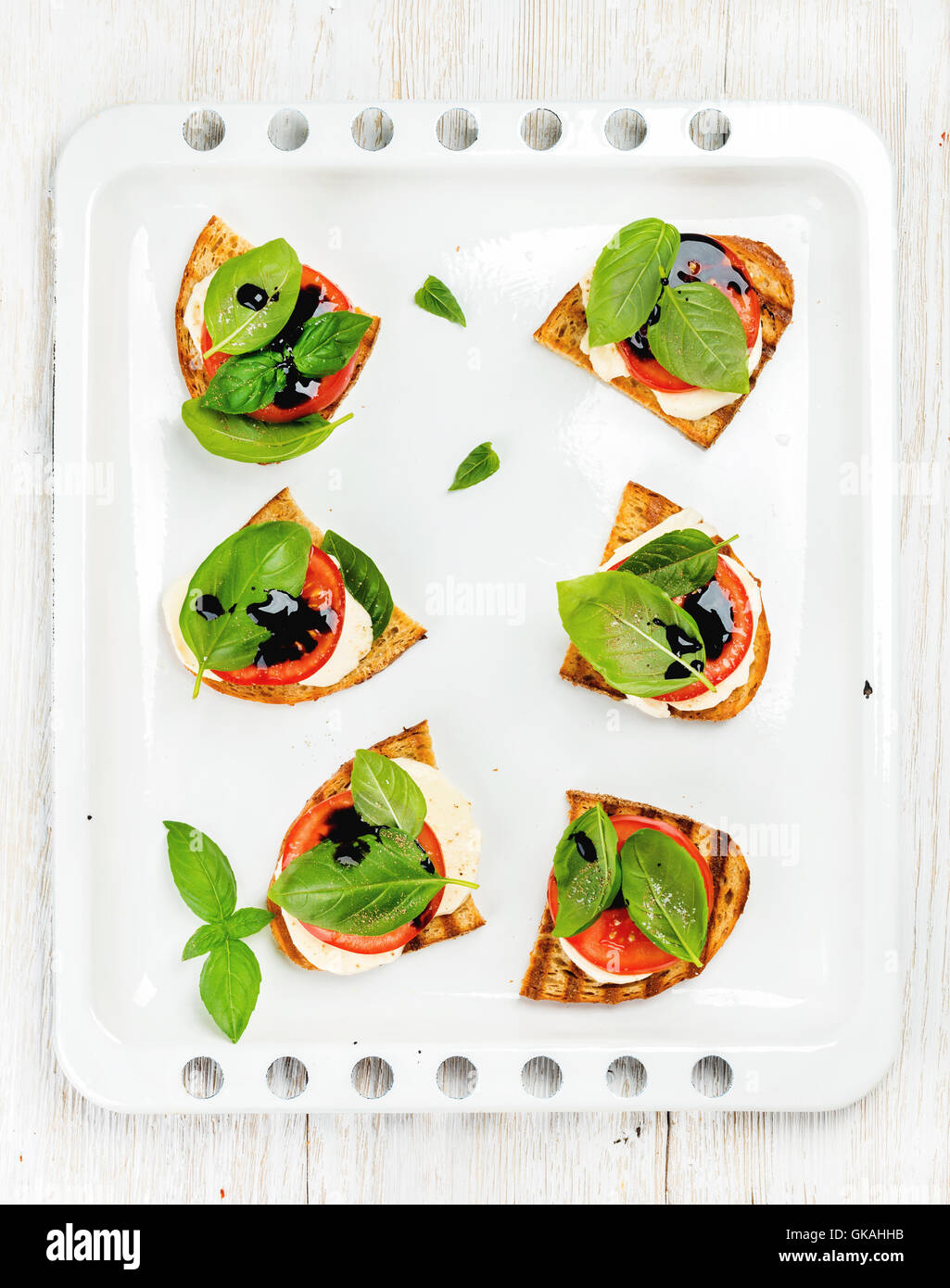 Caprese sandwiches with tomato, mozzarella cheese, basil and balsamic glaze on white baking tray