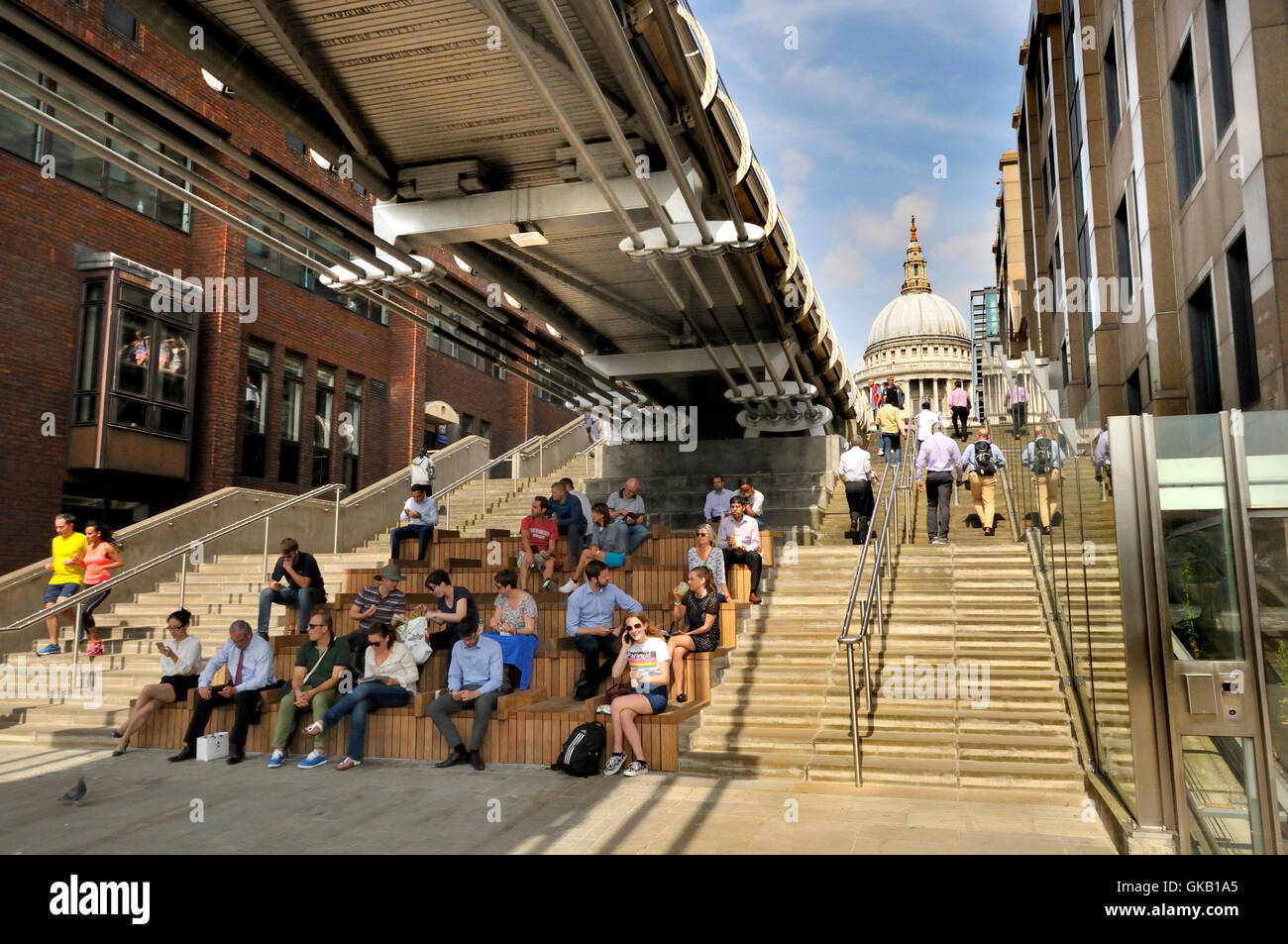 London England, UK. Lunchtime - people sitting under the Millennium Bridge, St Paul's Cathedral behind Stock Photo