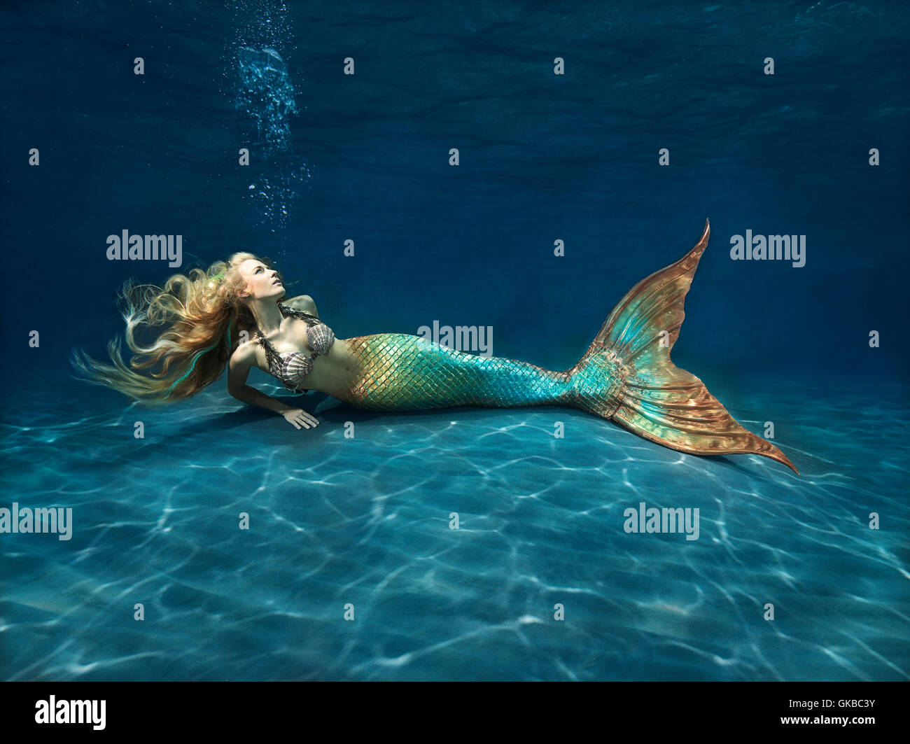 Young blonde mermaid laying on the ocean floor Stock Photo