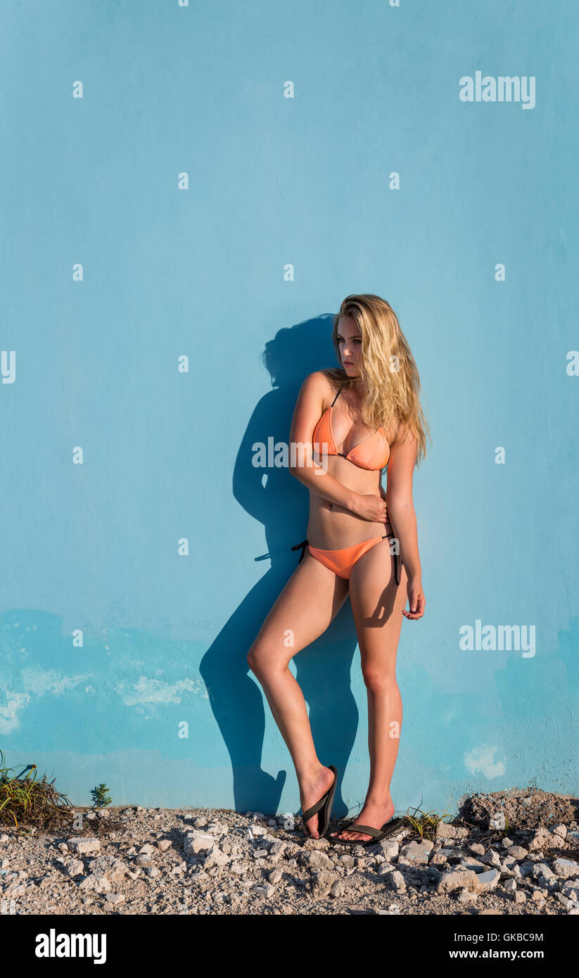 Young blonde model in an orange bikini against a blue wall, Isla Mujeres, Mexico Stock Photo