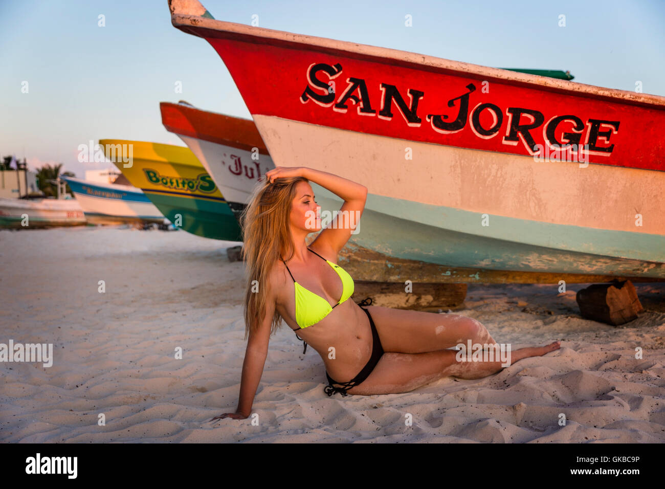 Young blond model on the beach by some rowboats at sunset, Isla Mujeres, Mexico Stock Photo