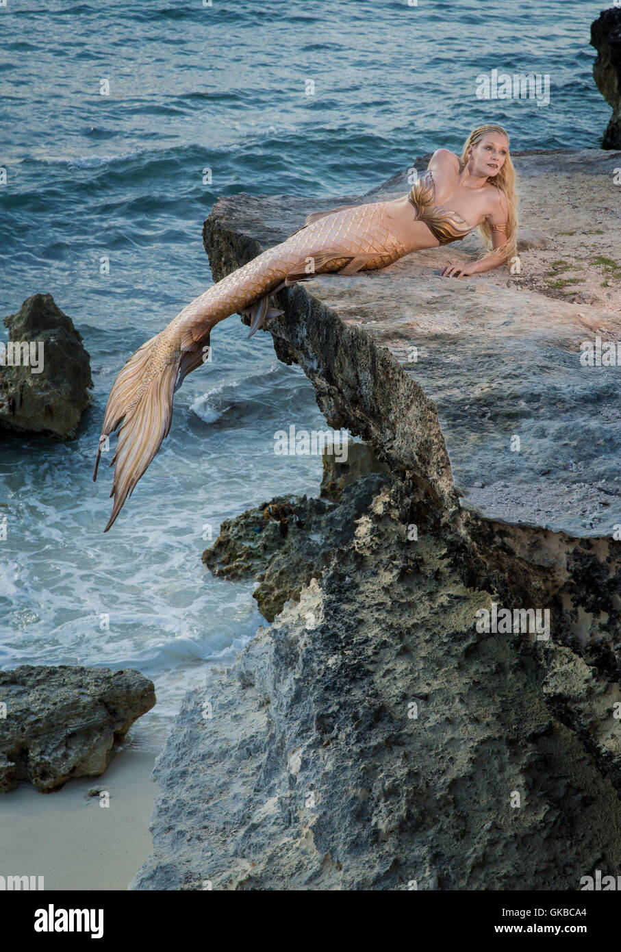 Blonde mermaid on the rocks above the beach Stock Photo