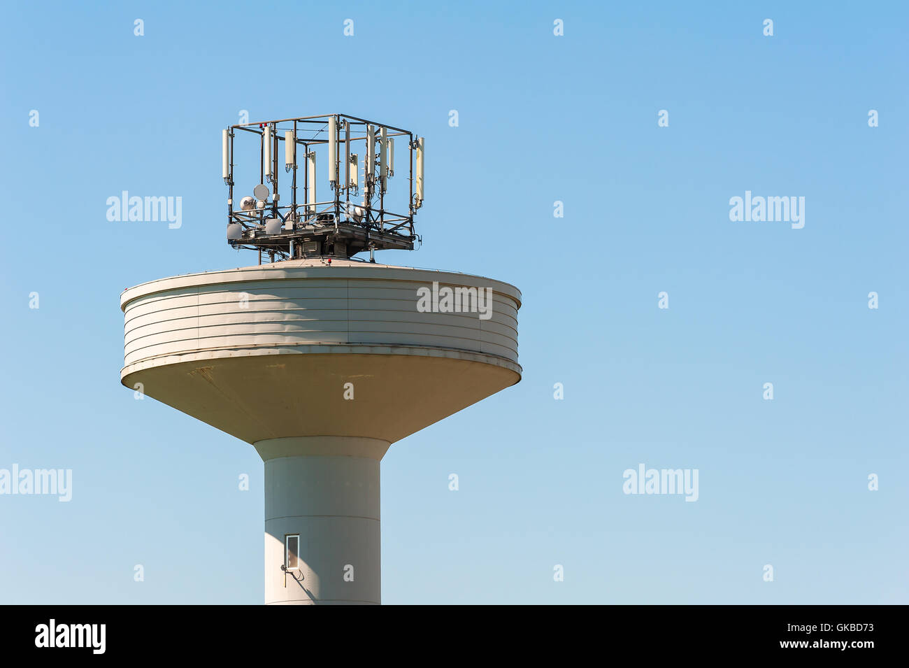 Water tank tower surmounted with a telephone repeater antennas against blue sky .Copy space Stock Photo