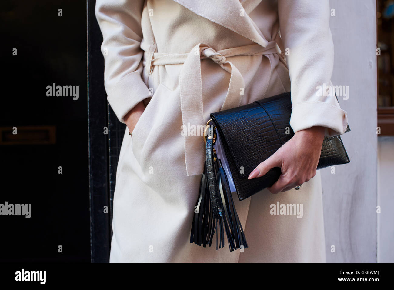 Mid section crop of woman in belted coat holding clutch bag Stock Photo