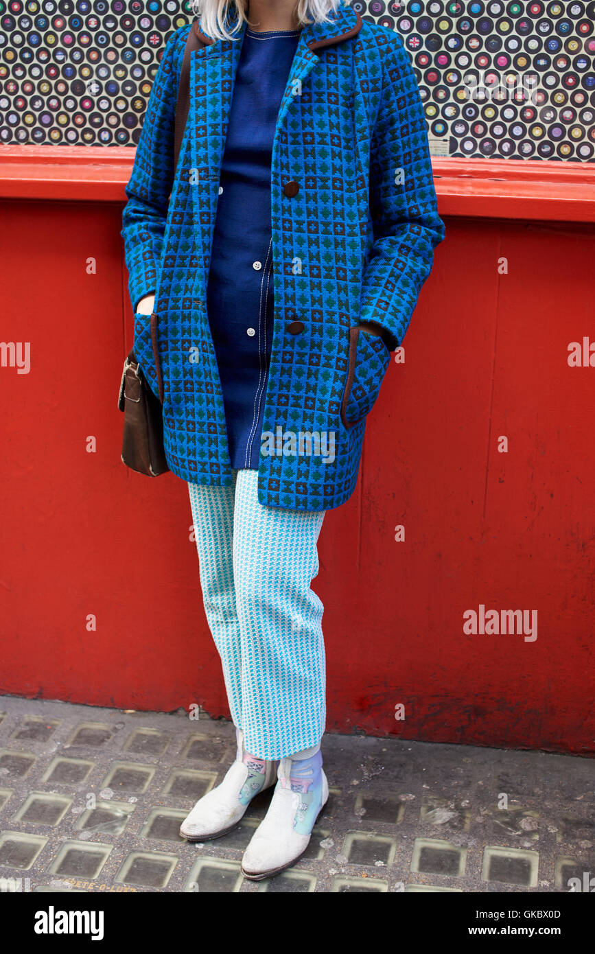 Woman against red wall wearing retro style coat and trousers Stock Photo