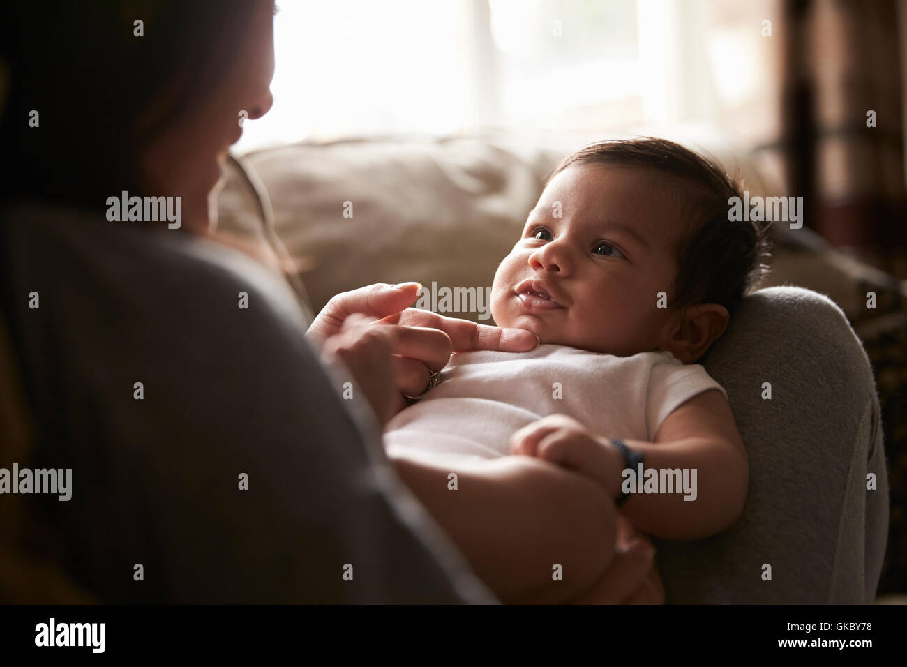Close Up Of Mother Playing With Baby Boy Lying On Sofa Stock Photo