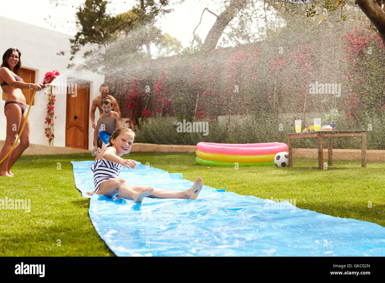 Family Having Fun On Water Slide In Garden Stock Photo