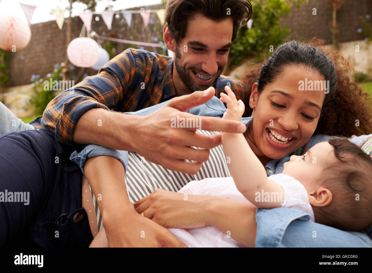 Family With Baby Playing On Rug In Garden Together Stock Photo