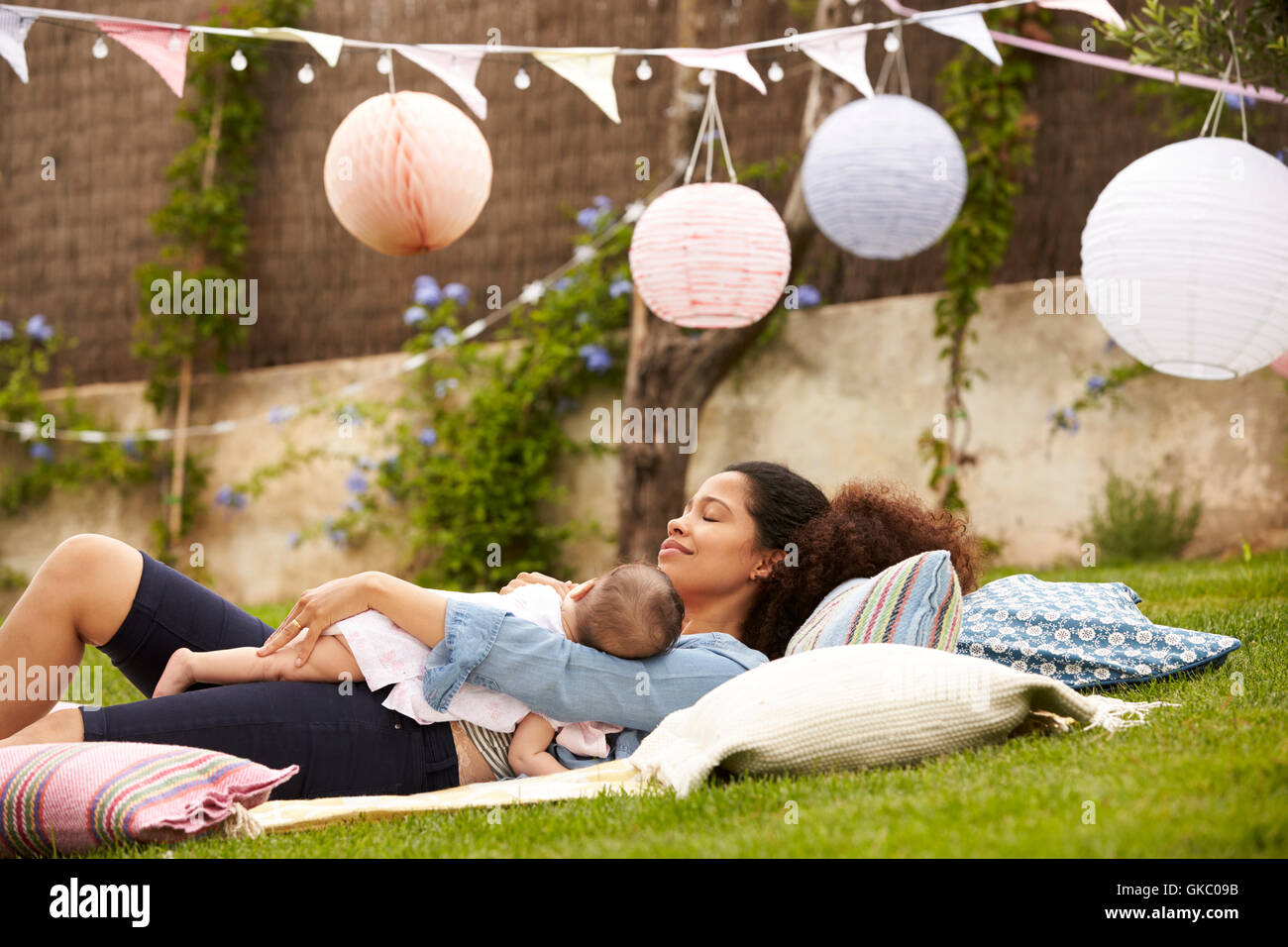 Mother With Baby Relaxing On Rug In Garden Together Stock Photo