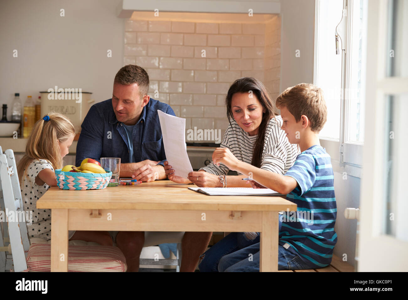 Parents Helping Children With Homework At Kitchen Table Stock Photo