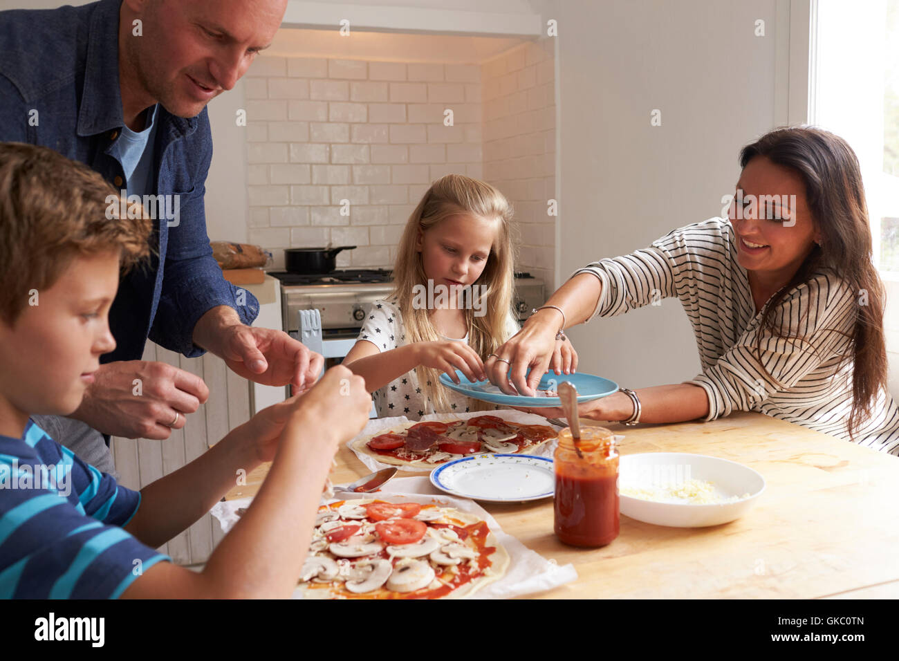 Family At Home In Kitchen Making Pizzas Together Stock Photo