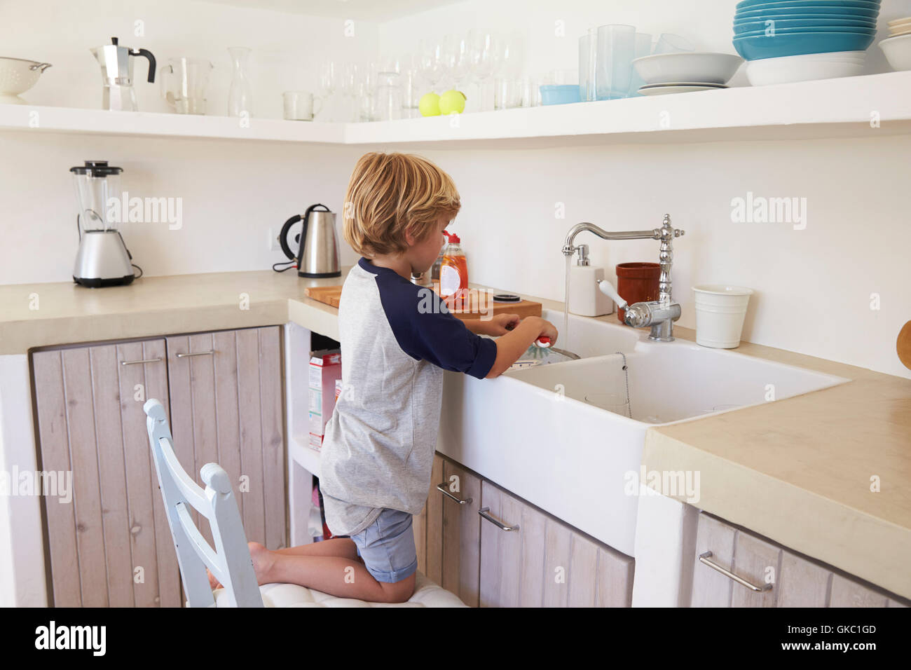 Young boy kneeling on a chair to wash dishes, full length Stock Photo