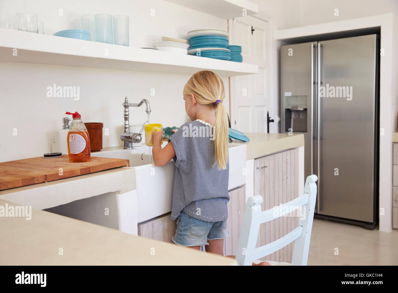 Young girl kneeling on chair washing up, back view Stock Photo