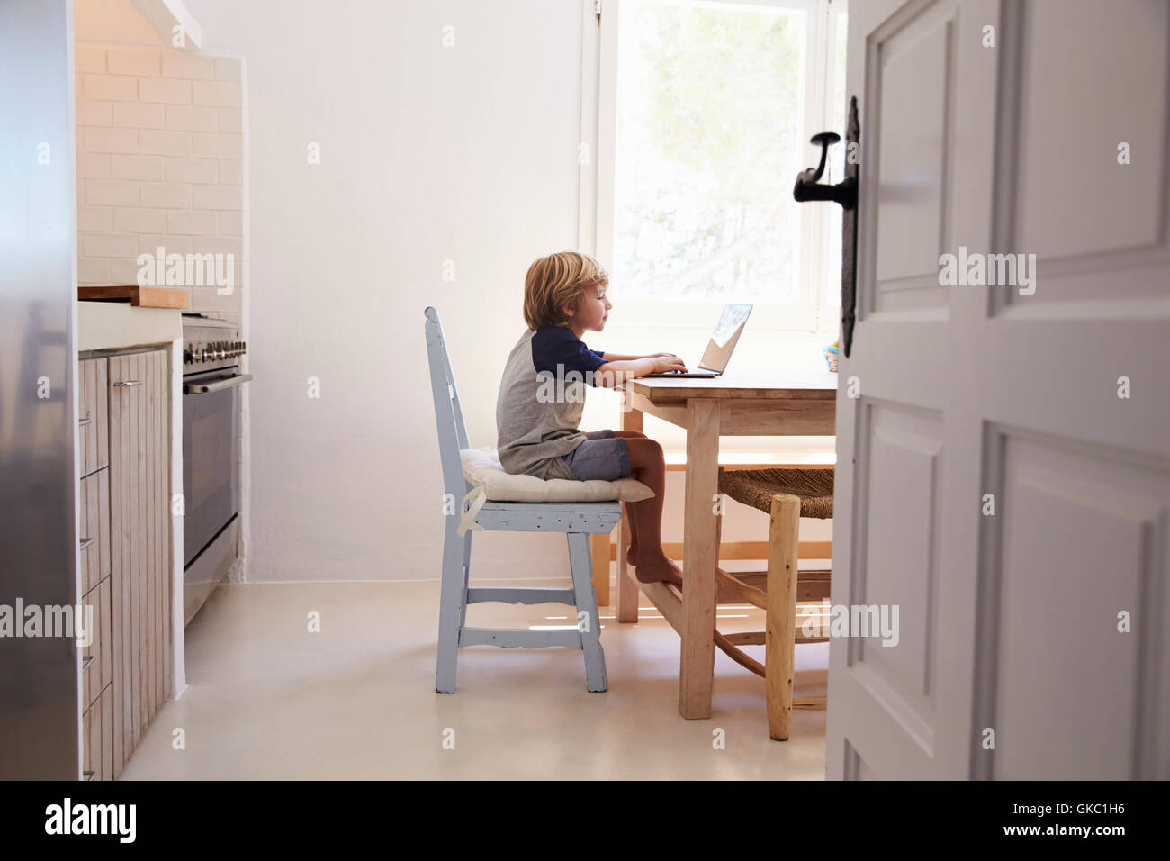 Young boy using laptop in kitchen, side view, from doorway Stock Photo