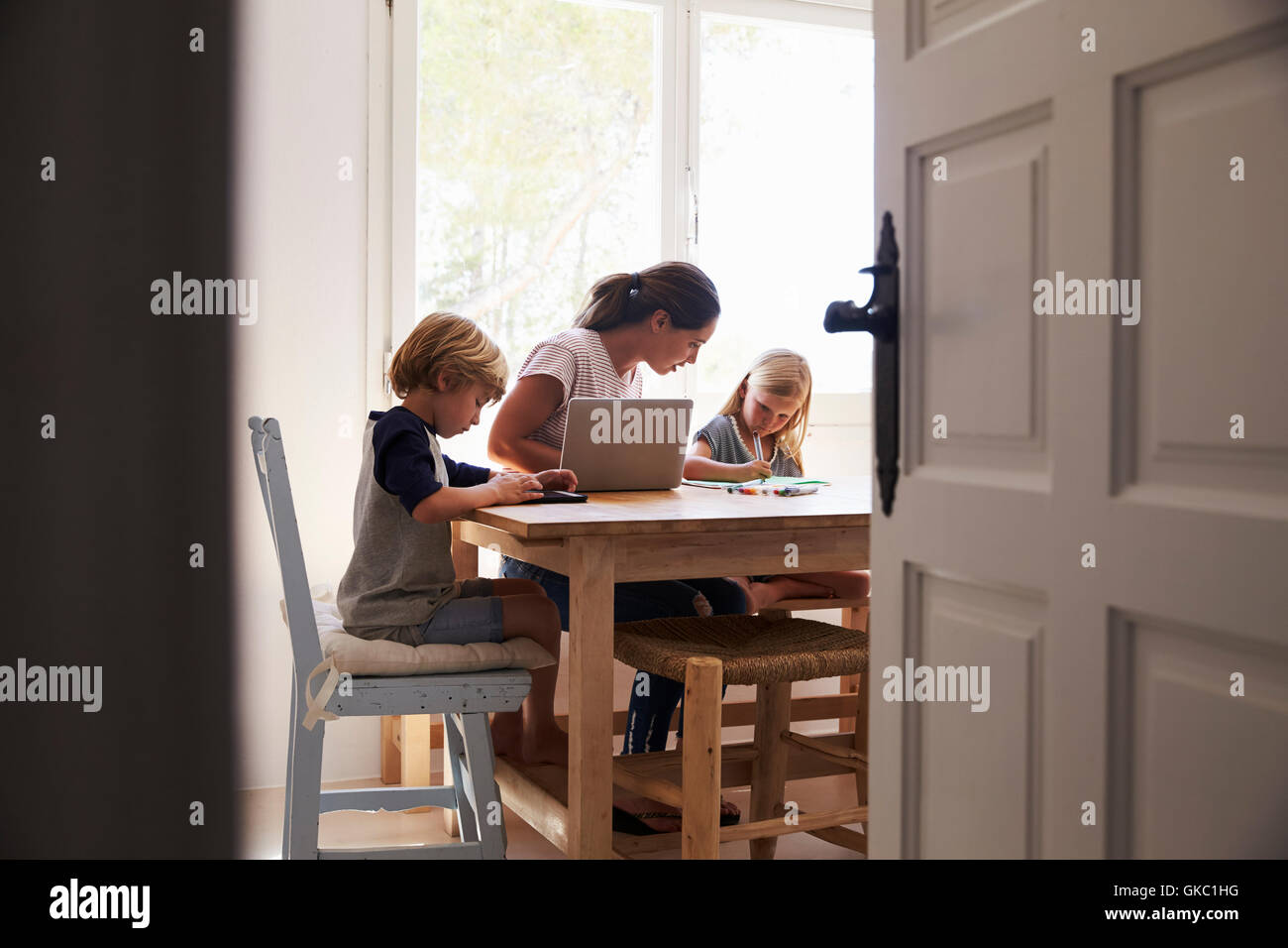 Mum and two kids working in kitchen, close up from doorway Stock Photo