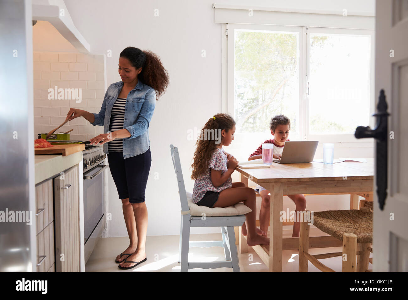 Mum cooking while kids work at kitchen table, from doorway Stock Photo