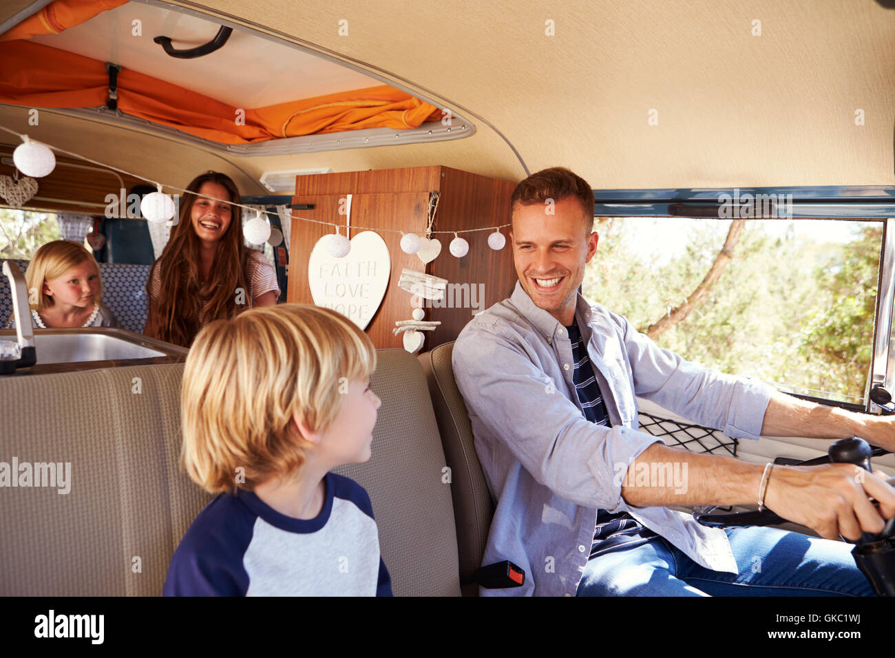 Dad driving family in a camper van, looking at his son Stock Photo Alamy