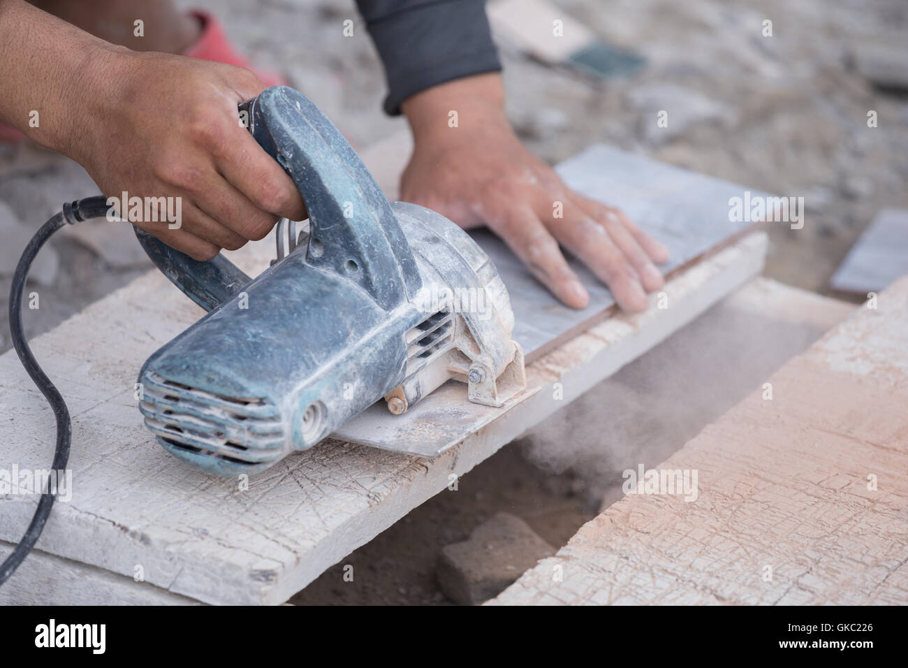 worker cutting a tile using an angle grinder at construction site Stock
