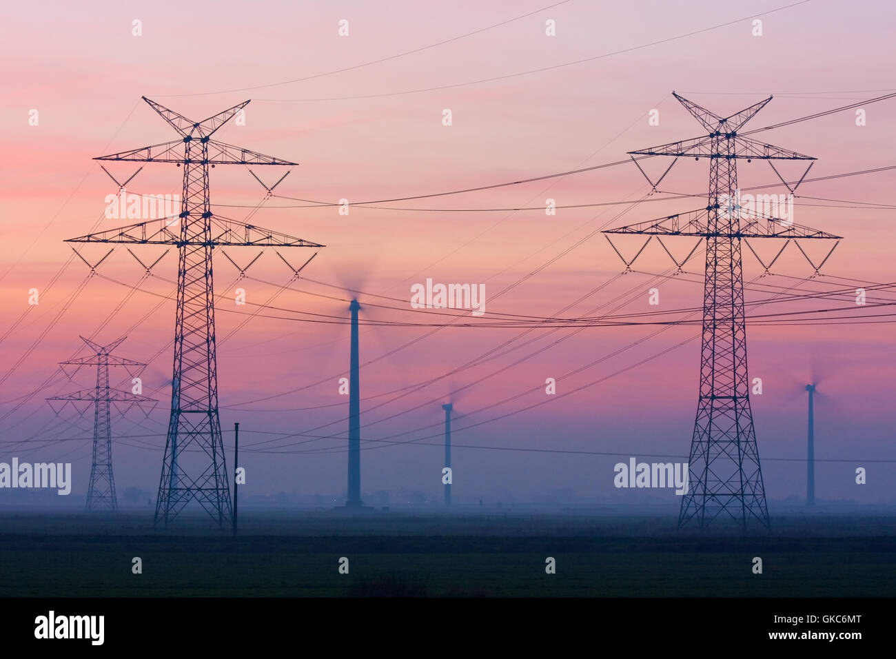 electricity pylons and wind turbines at dusk Stock Photo