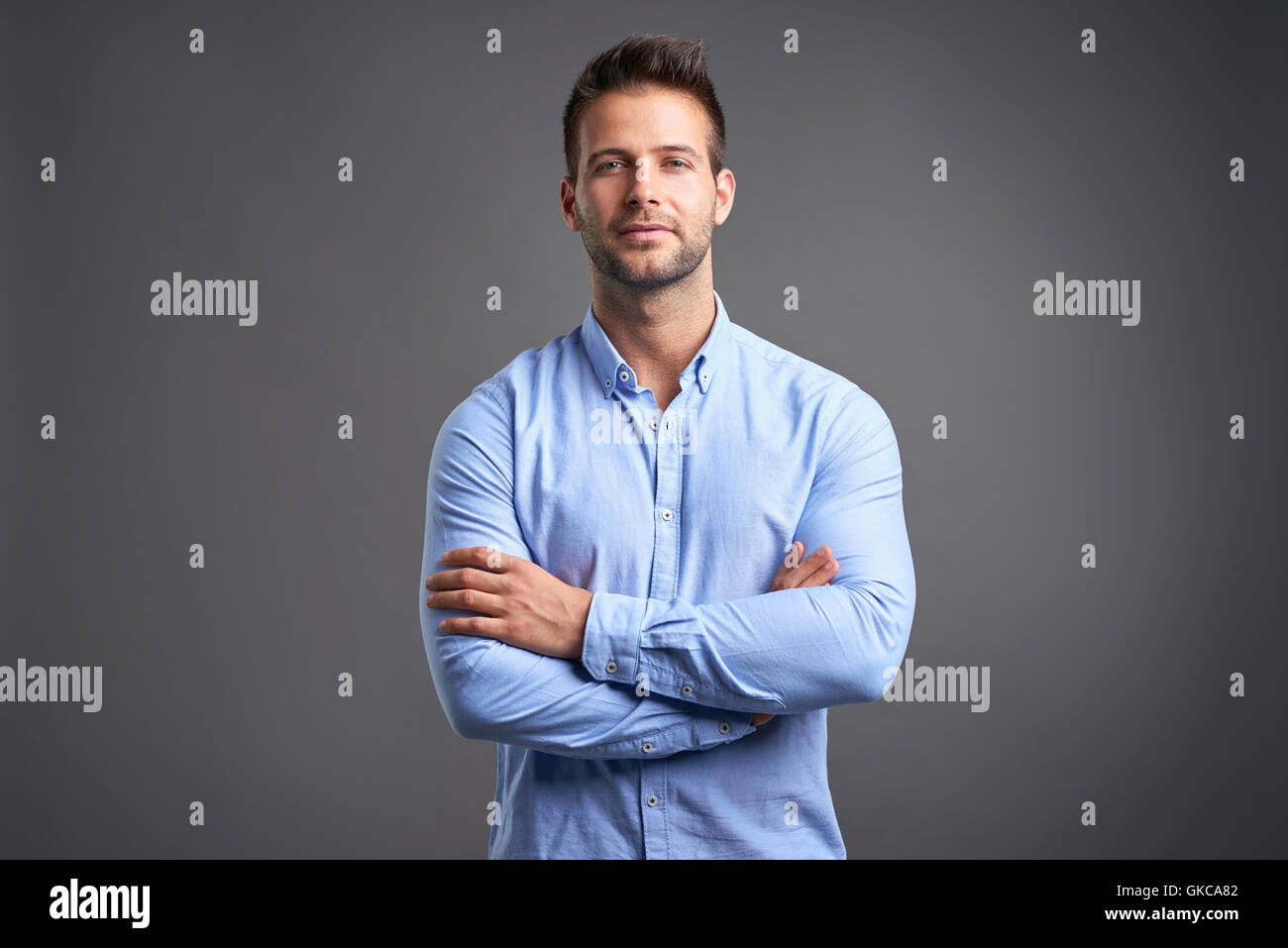 A confident handsome young man standing in front of a grey background ...