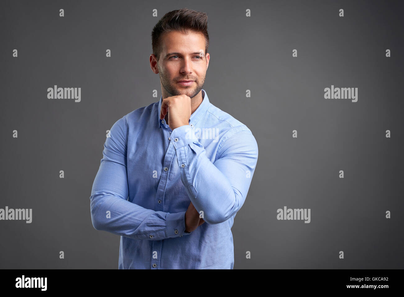 A confident handsome young man standing in front of a grey background ...