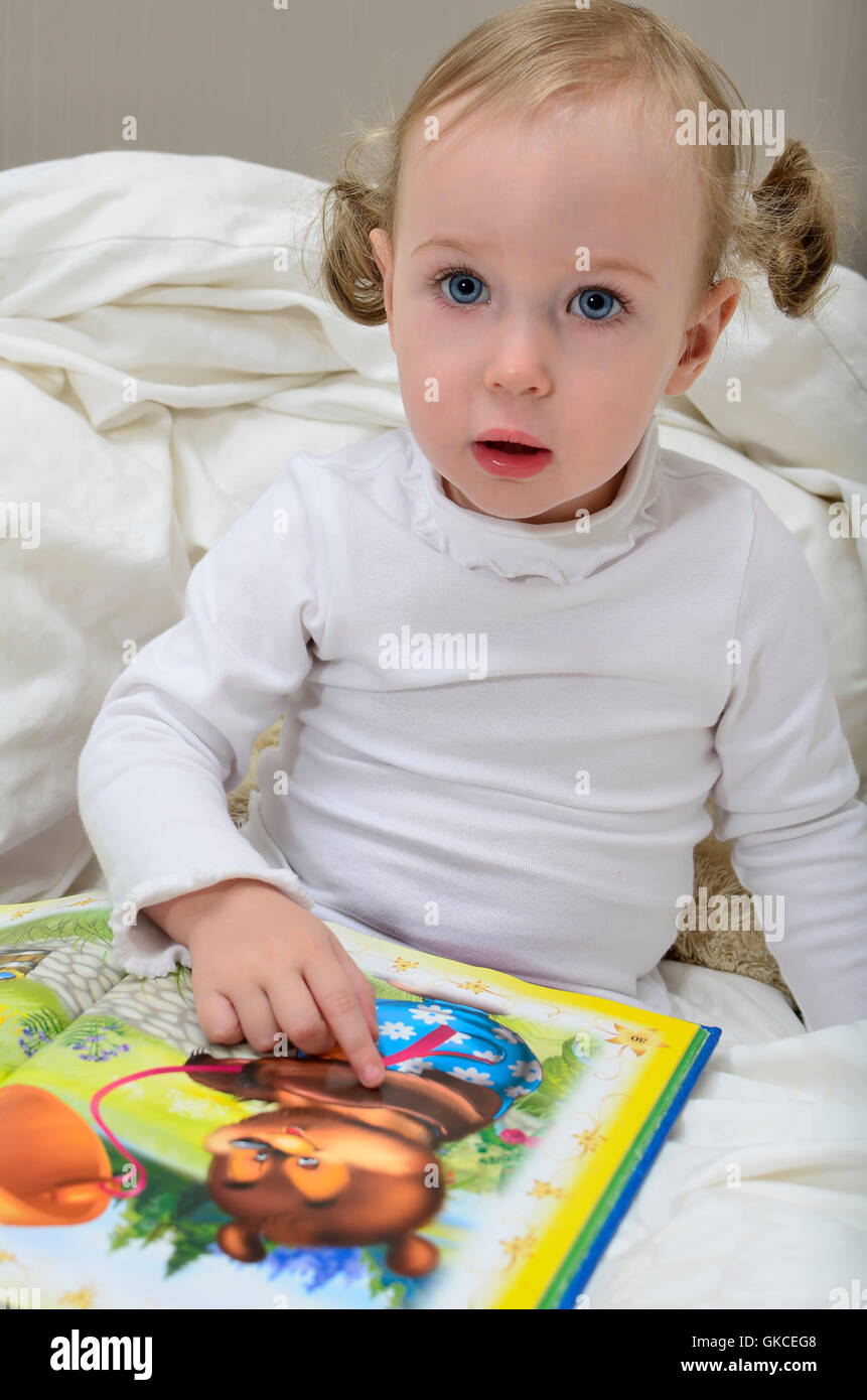 little girl sitting on the bed and reading a book Stock Photo - Alamy