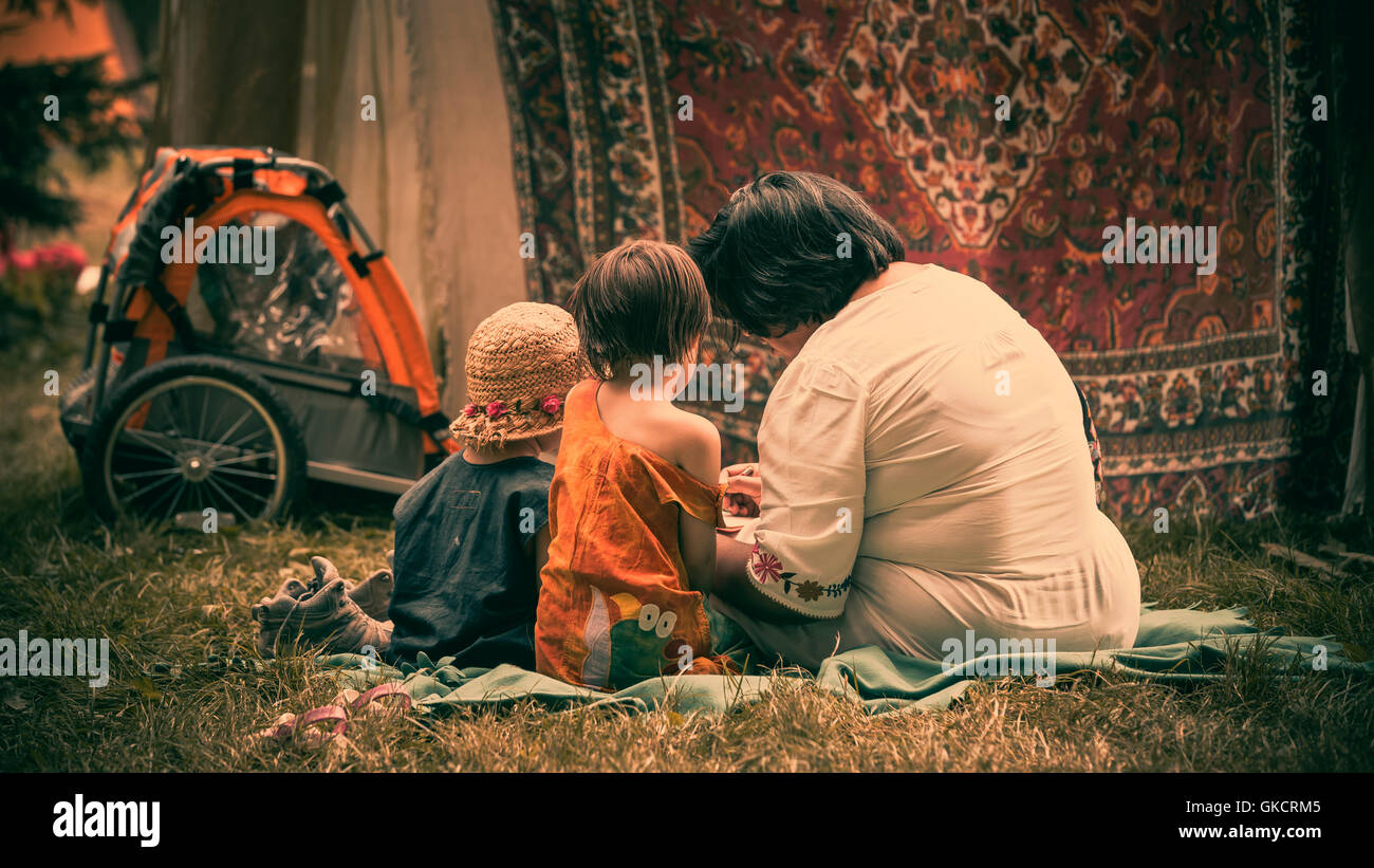 A woman and two children are involved in reading sitting on a picnic blanket surrounded by tents at WOMAD festival, UK Stock Photo
