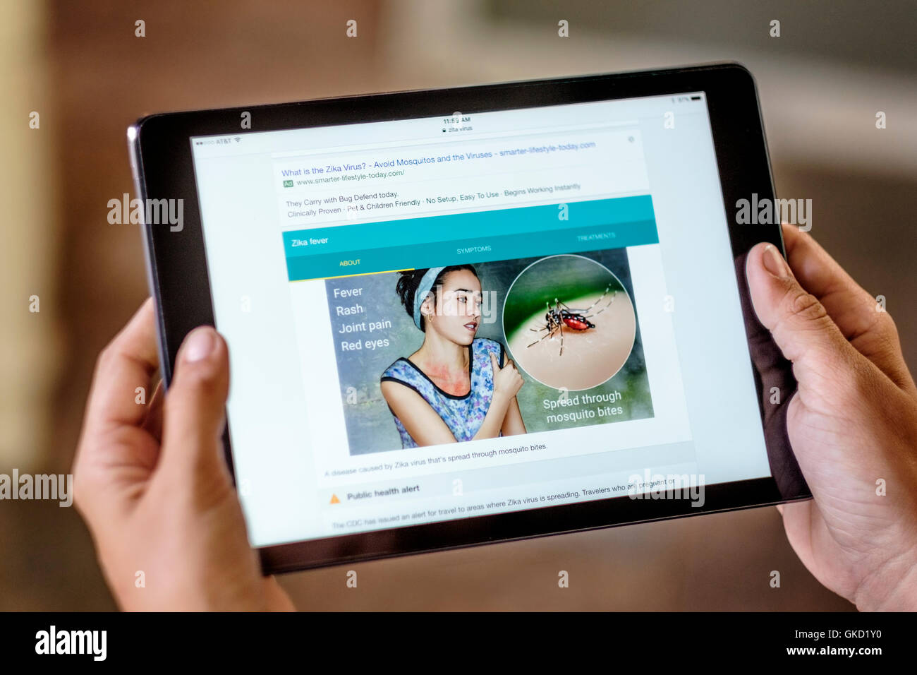 A young woman's hands hold an iPad researching the Zika virus. Closeup. Stock Photo