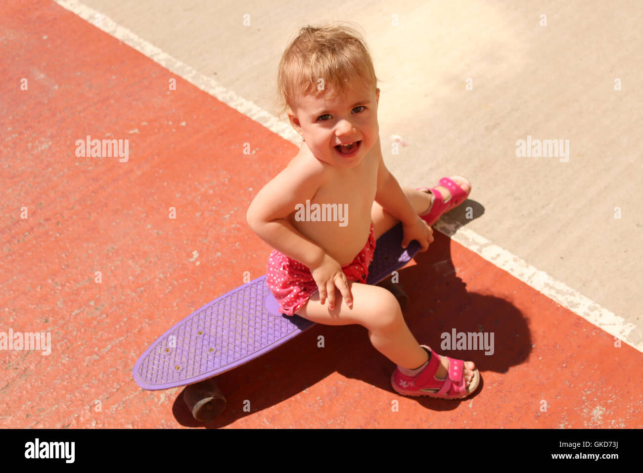 small child in shorts sitting on a skateboard summer sunny day Stock Photo
