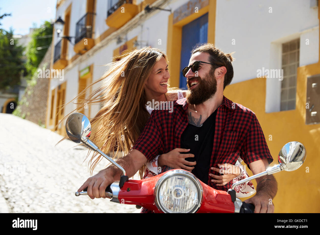 Couple sitting on motor scooter looking at each other, Ibiza Stock Photo