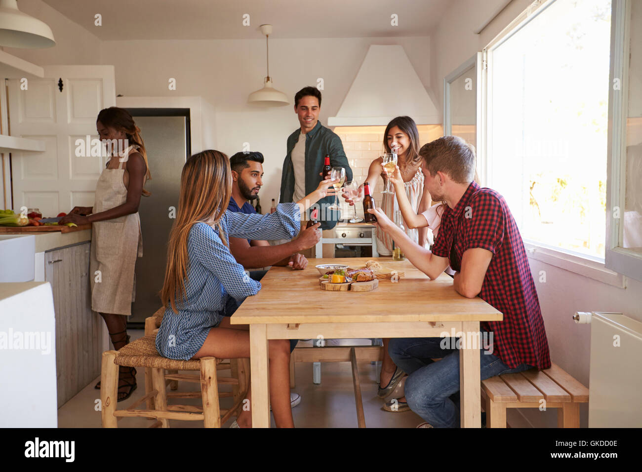 Friends making a toast in kitchen, one preparing food Stock Photo