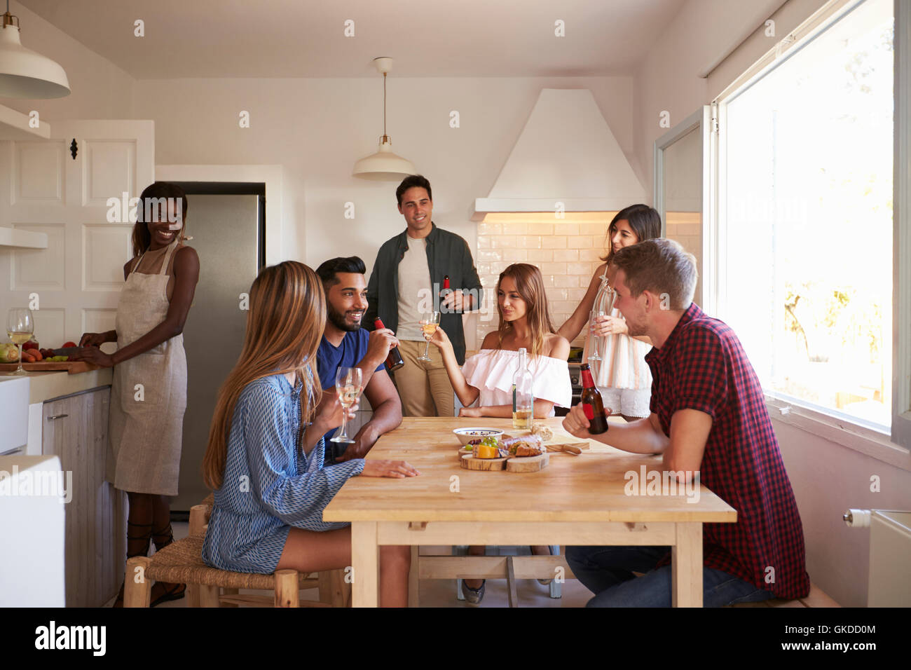 Group of friends talk in kitchen, one preparing food Stock Photo