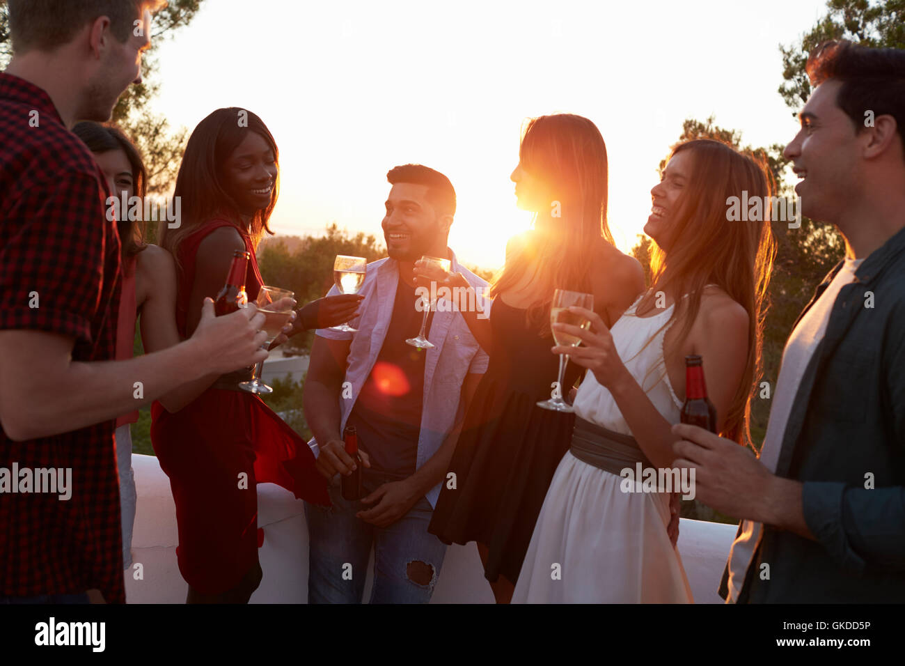 Adult friends socialising at a party on a rooftop at sunset Stock Photo