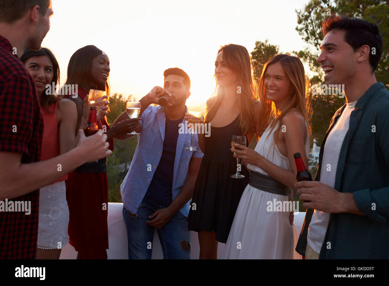 Adult friends socialising at a party on a rooftop at sunset Stock Photo