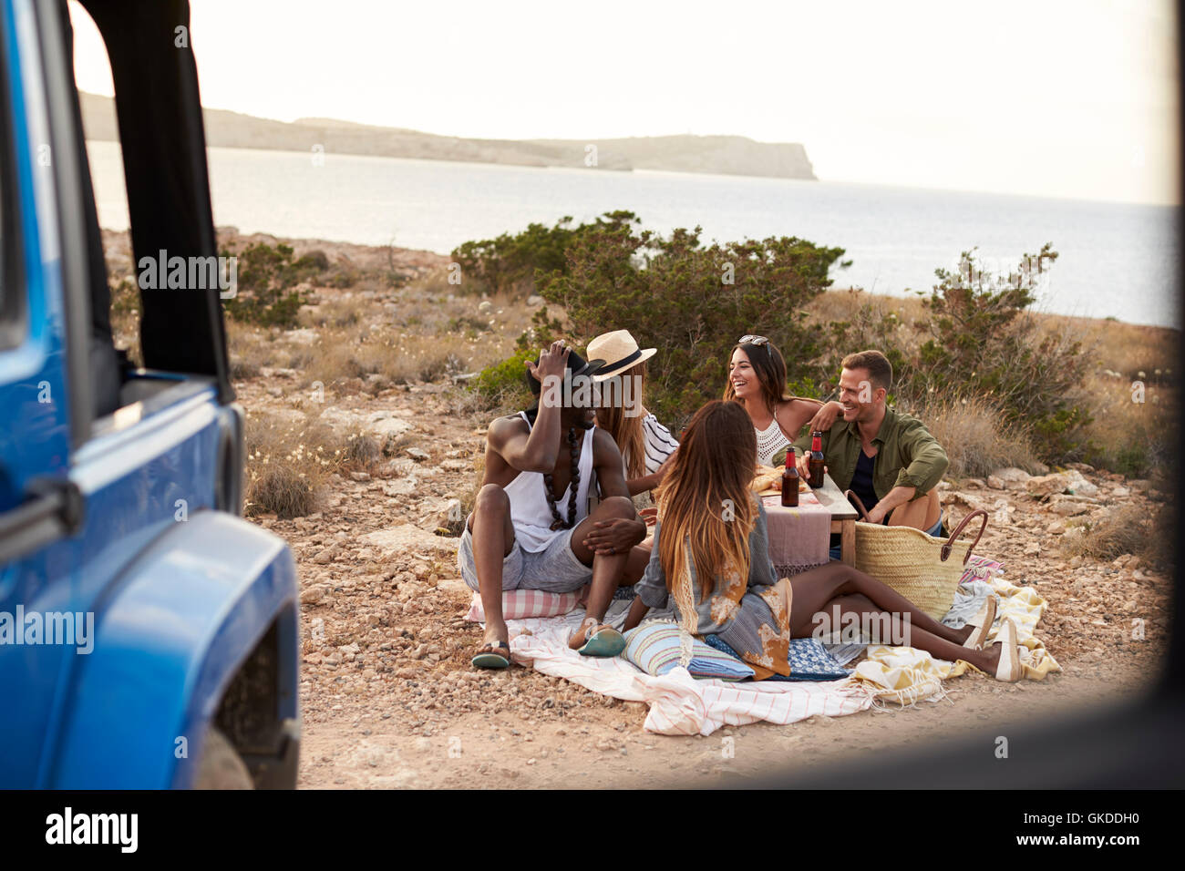 Group Of Friends Enjoying Picnic On Cliffs By Sea Stock Photo