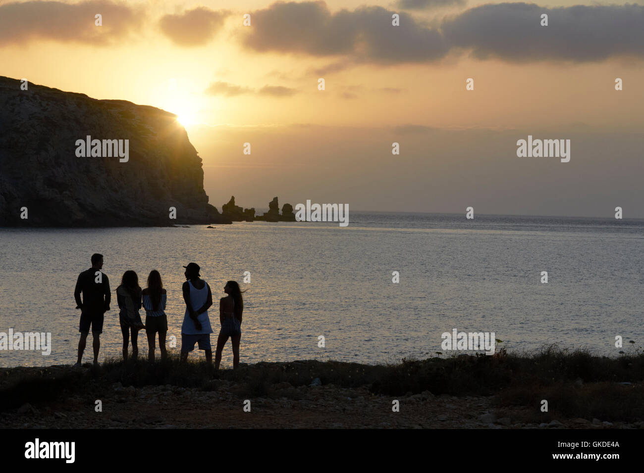 Rear View Of Friends Standing On Cliff Watching Sunset Stock Photo