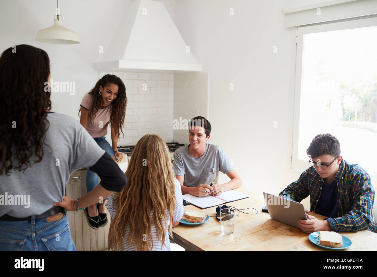 Teens hanging out in kitchen, doing homework and talking Stock Photo