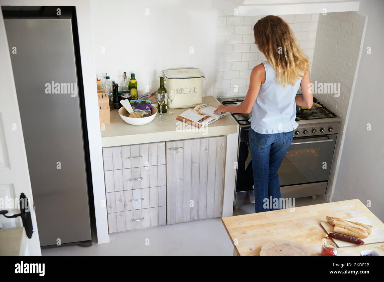 Back view of woman cooking in kitchen, reading recipe book Stock Photo