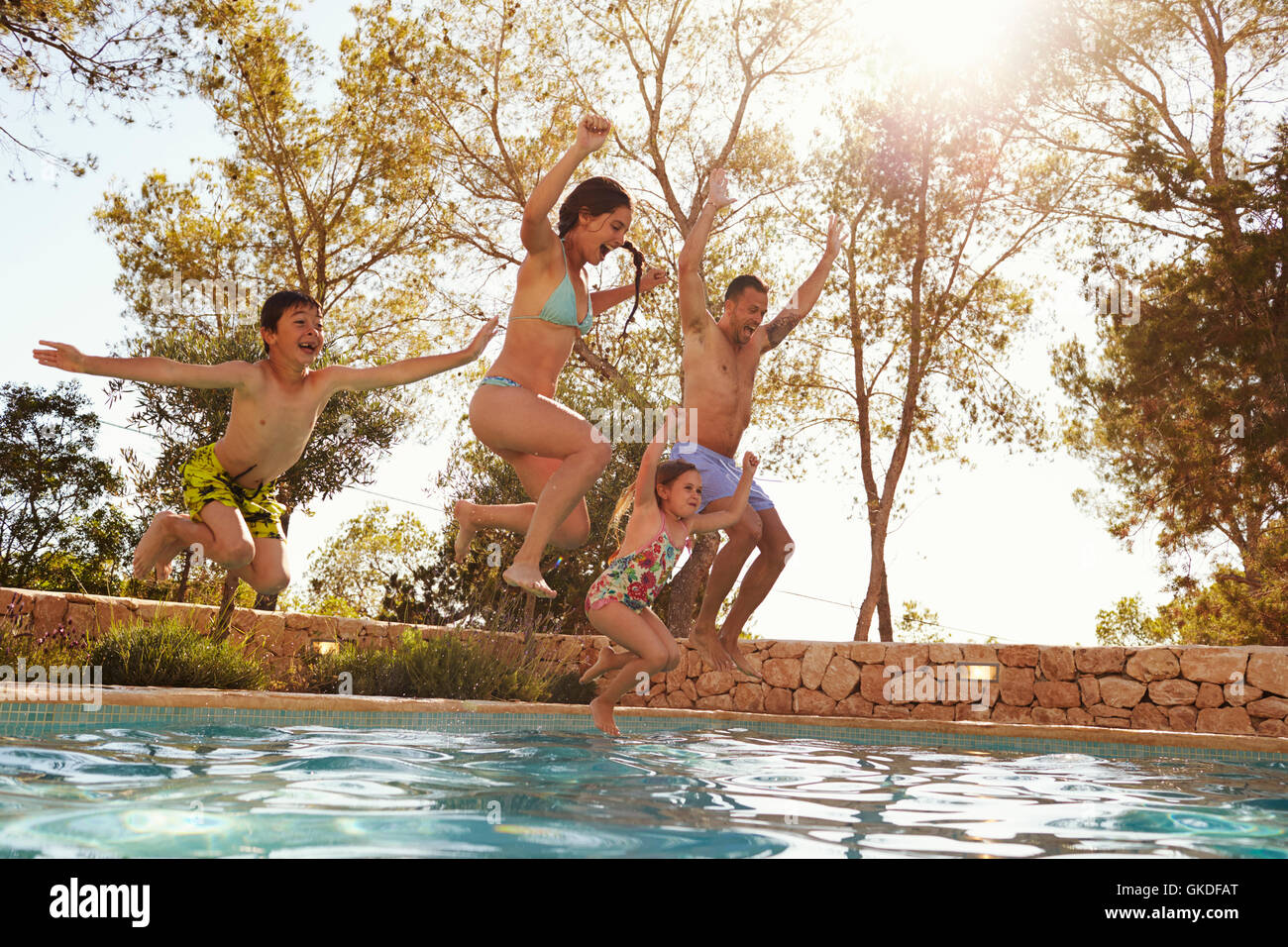 Family On Vacation Jumping Into Outdoor Pool Stock Photo