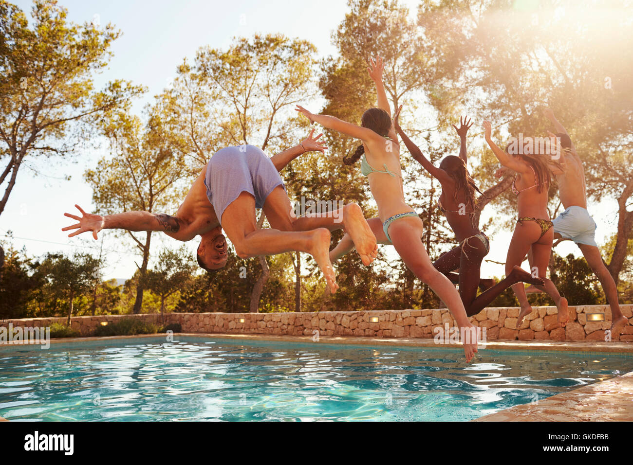 Group Of Friends On Vacation Jumping Into Outdoor Pool Stock Photo