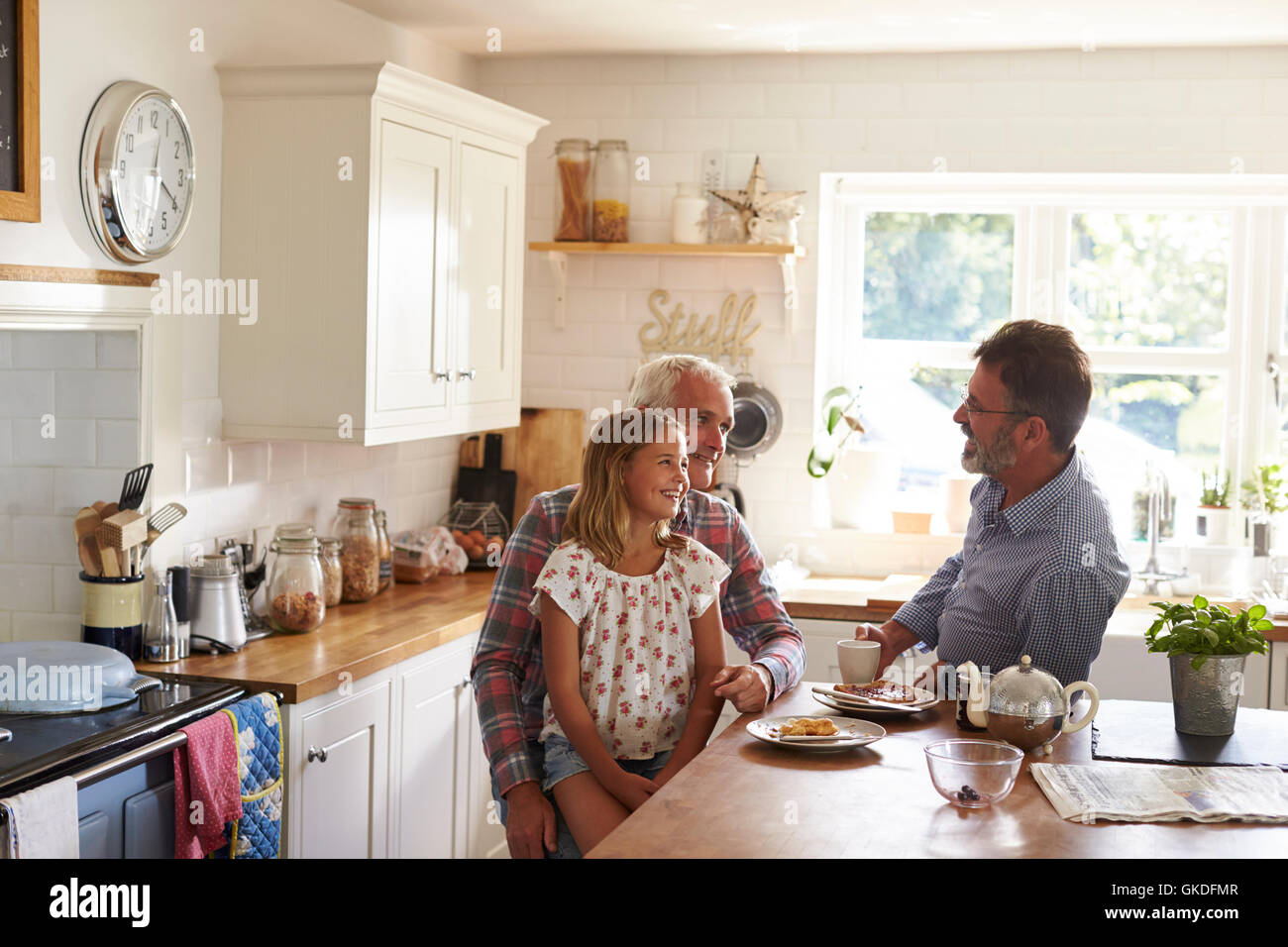 Smiling girl sits on knee, talking with dads at breakfast Stock Photo