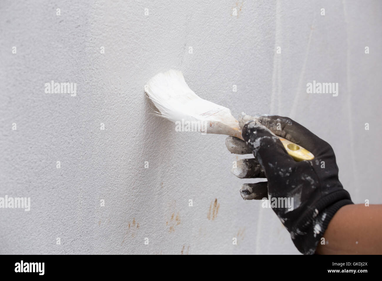 Hand holding brush painting white color to the concrete wall Stock