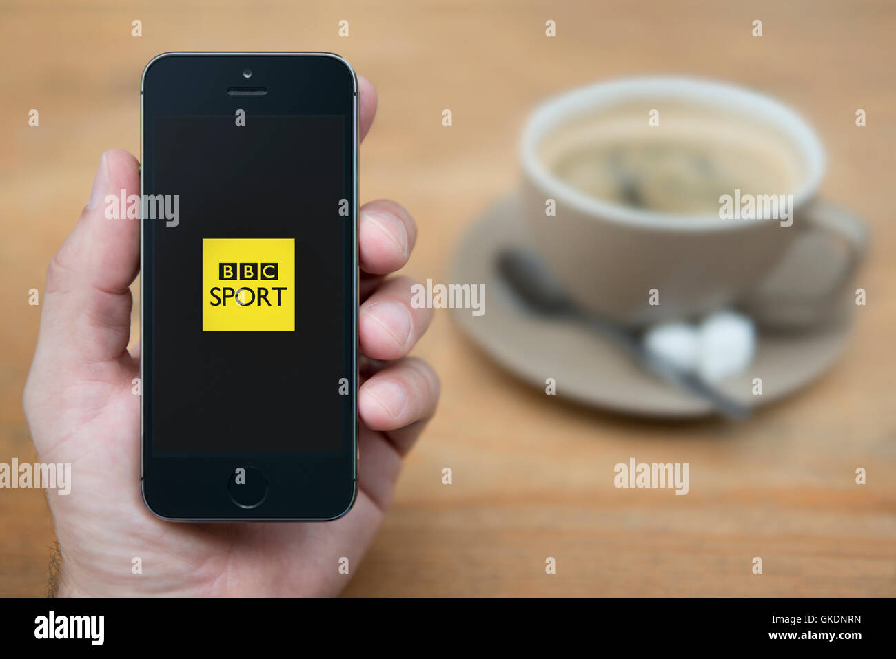 A man looks at his iPhone which displays the BBC Sport logo, while sat with a cup of coffee (Editorial use only). Stock Photo