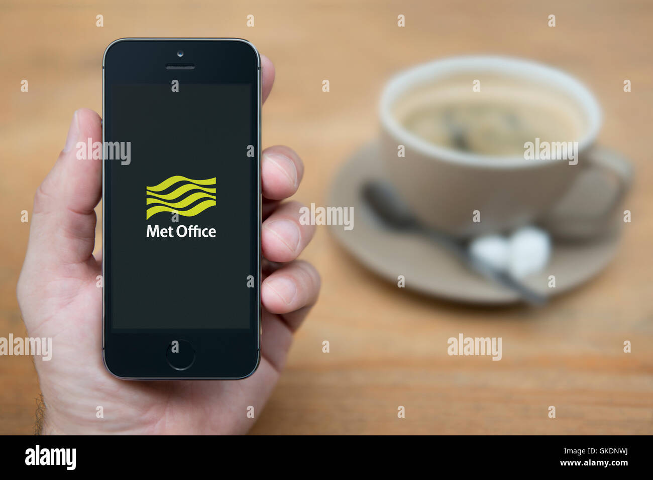 A man looks at his iPhone which displays the Met Office logo, while sat with a cup of coffee (Editorial use only). Stock Photo