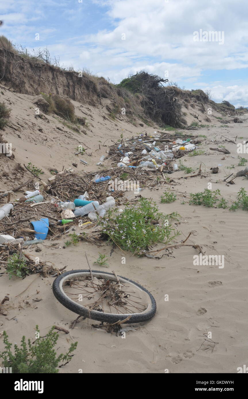 This is washed up rubbish on a sandy beach including plastic bottles a bicycle wheel, rope, food containers Stock Photo