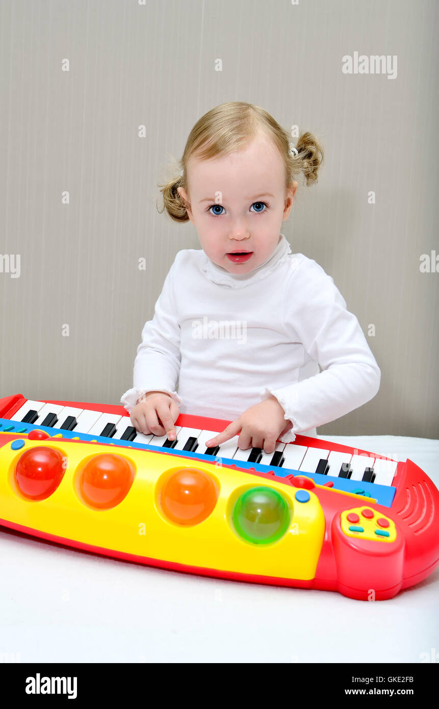 little girl sitting on the bed and plays on a children's keyboard Stock Photo