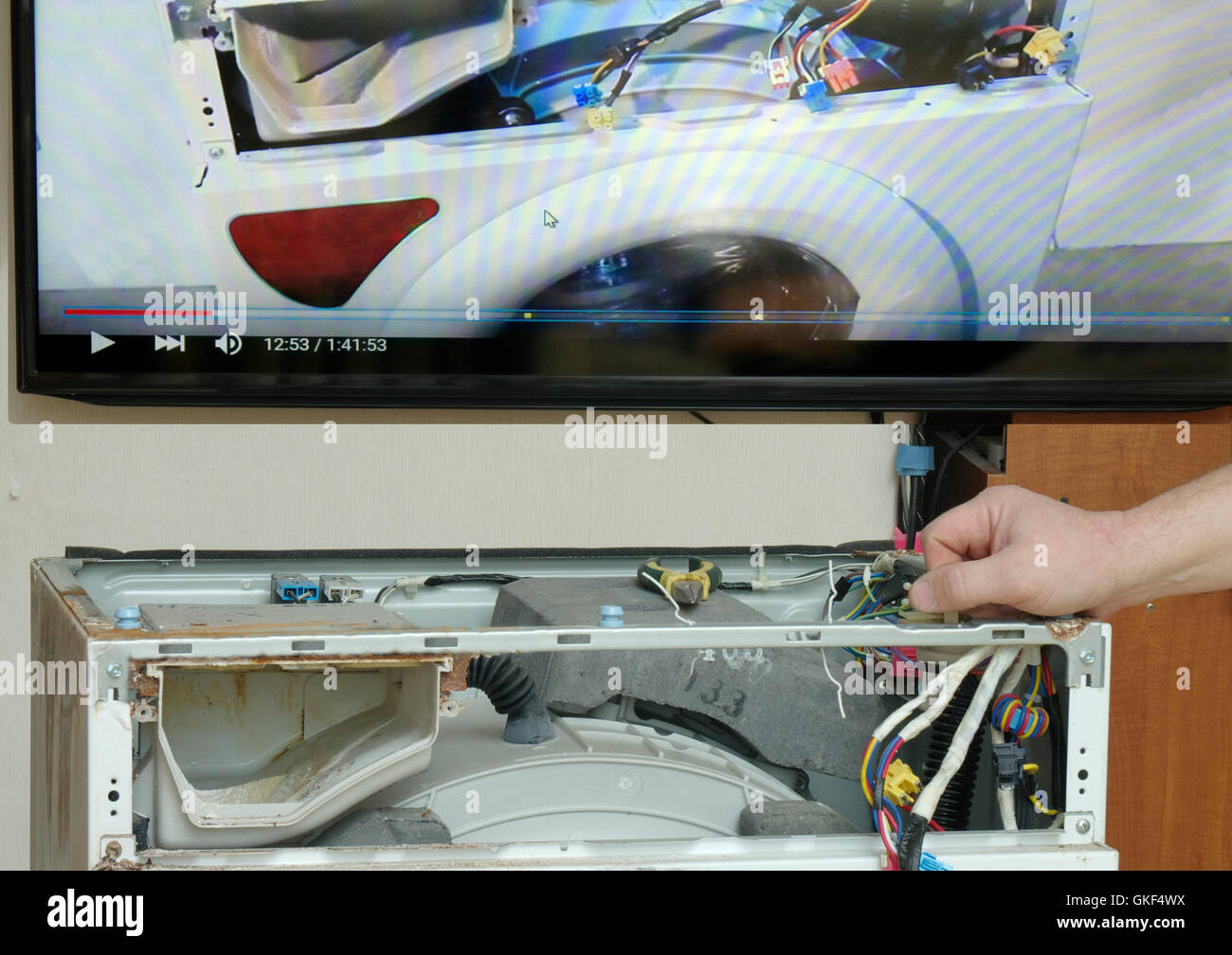 Repairman is repairing a washing machine, using the video instructions on the TV ,repair their own hands Stock Photo