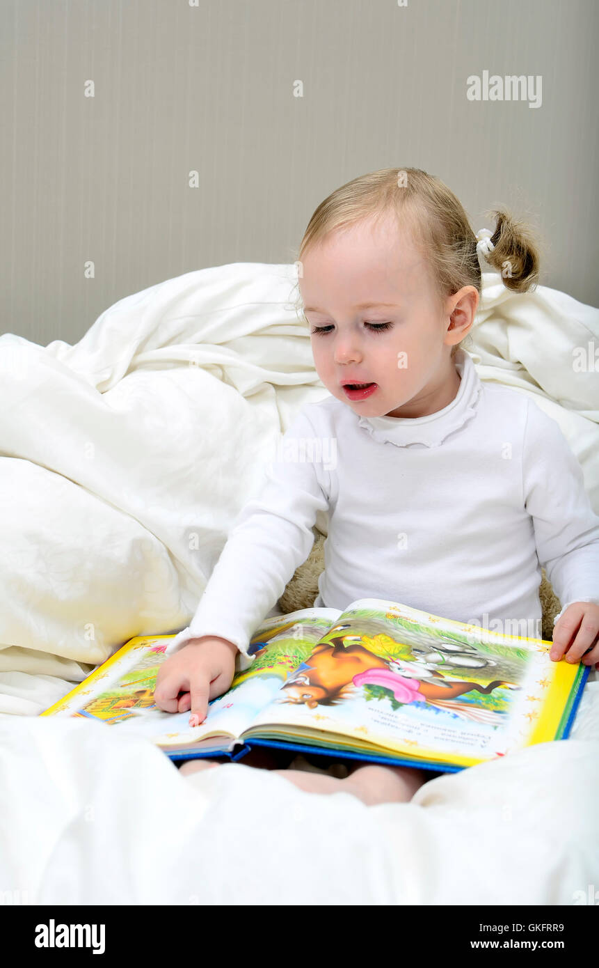 little girl sitting on the bed and reading a book Stock Photo - Alamy