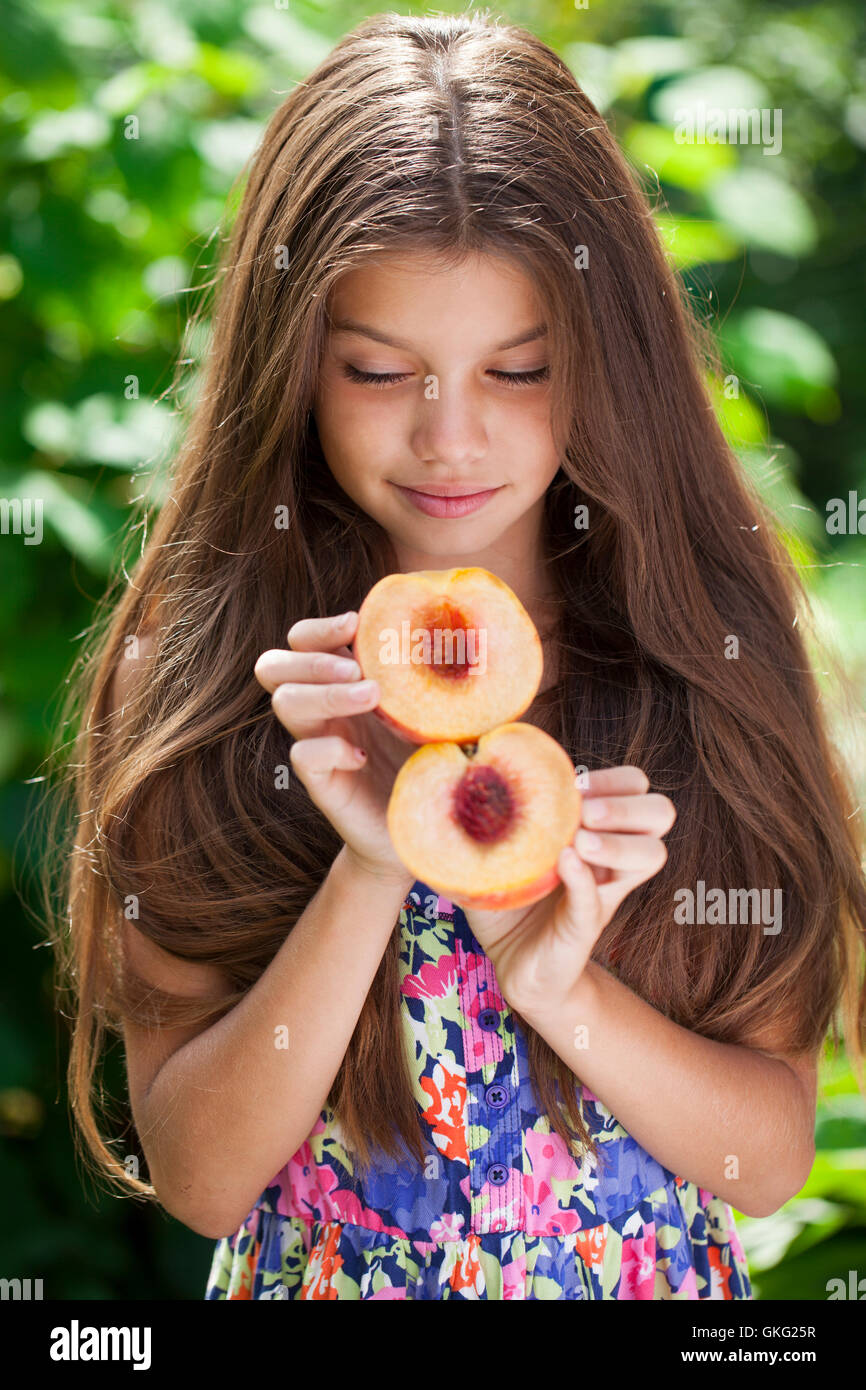 Portrait of a young brunette little girl with peach, summer outdoor