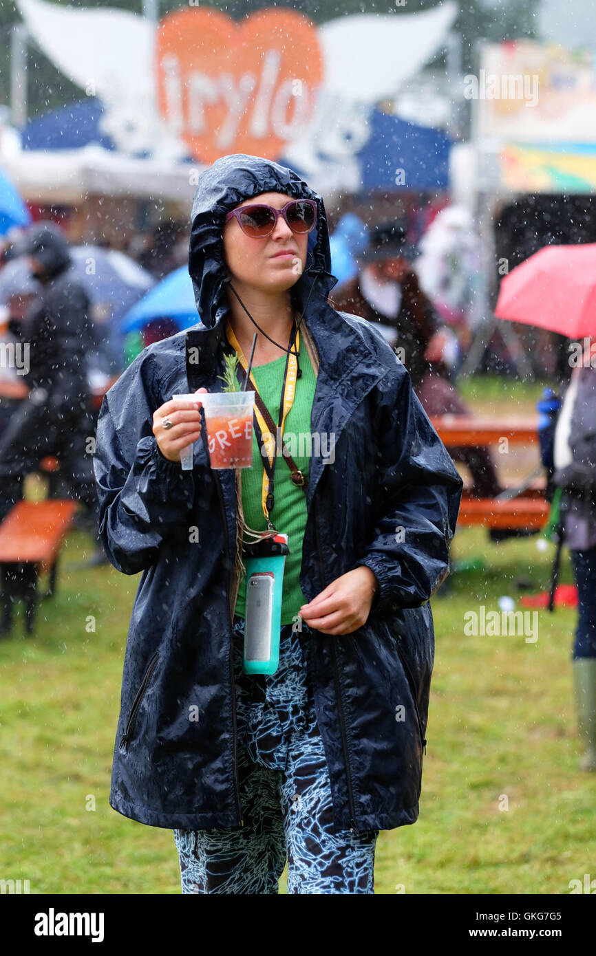 Green Man Festival, Crickhowell, Wales  - August 2016 - Rain and more rain at the Green Man Festival with occasional moments of sunshine - A fan does her best to stay dry to enjoy her cocktail. Stock Photo